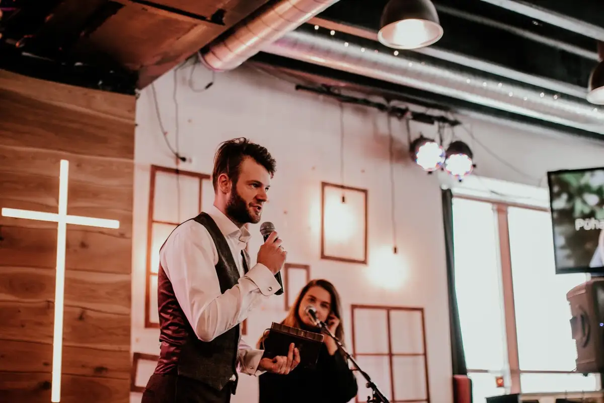 A preacher with a microphone by the wooden wall and the cross